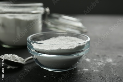 Baking powder in bowl and spoon on black textured table, closeup. Space for text