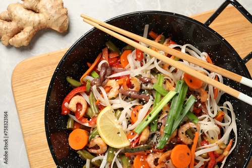 Shrimp stir fry with noodles and vegetables in wok on grey table, top view