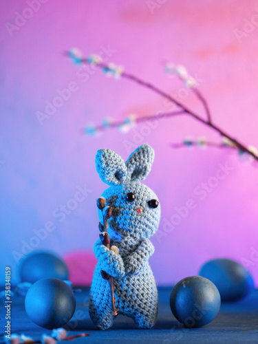 Happy Easter greeting card with a knitted bunny and blue Easter eggs. A bunny is holding a willow branch .