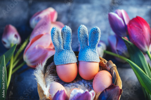 Easter eggs with bunny ears in a basket. Fresh pink and purple tulips.