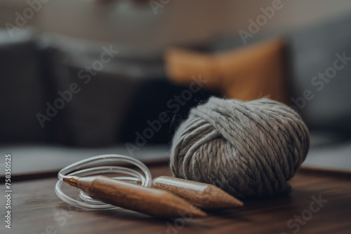 Ball of grey chunky wool yarn and large circular knitting needles on a wooden table.