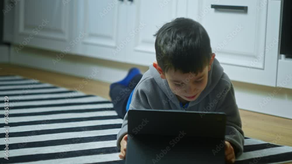 Curious cute kid boy lying on carpet floor using digital tablet device. Child surfing internet play game at home. Children tech addiction concept Curious cute kid boy lying on carpet floor using digital tablet device. Child surfing internet play game at home. Children tech addiction concept