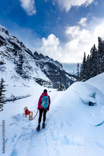 Backpacker Girl with her dog admires beautiful views of snow covered mountains near Lake Louise