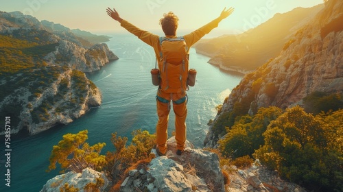 Person in orange stands on a cliff, arms wide, overlooking a breathtaking, sunlit coastal landscape