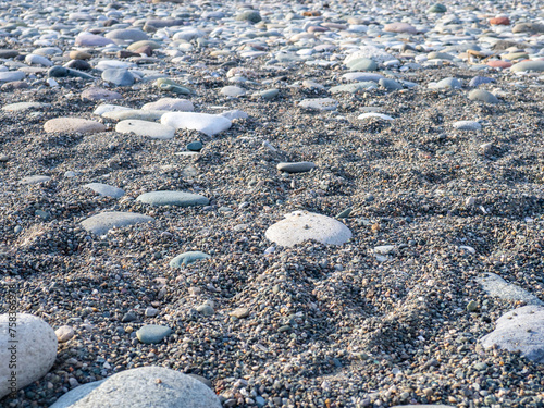 Gray sand and stones on the beach. Beach in winter. Sea coast soil.