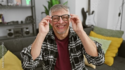 Wallpaper Mural Smiling senior man adjusting glasses in a cozy living room, personifying casual comfort and style. Torontodigital.ca