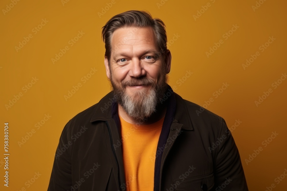 Portrait of a handsome middle-aged man with a beard and mustache in a black jacket and orange t-shirt on a yellow background
