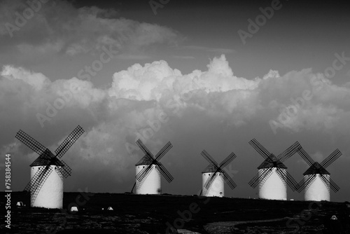 Traditional windmills lined up on a plain, their sails standing out against fluffy clouds, captured in stunning black and white photo