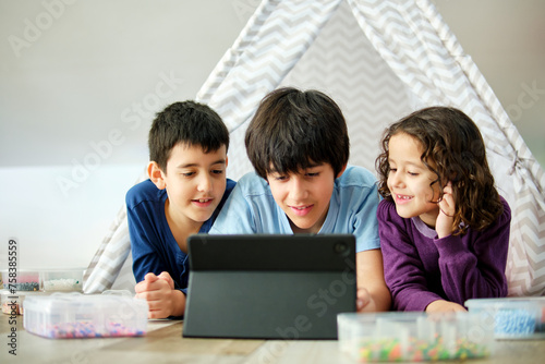 Siblings enjoying digital tablet with craft beads around