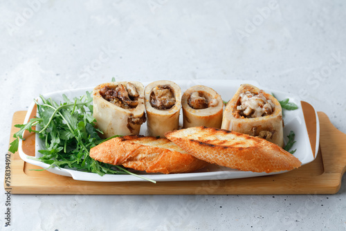 Homemade Roasted Beef Bone Marrow with bread crumbs, greens rocket arugula salad and croutons on plate, wooden board grey background. Top View.