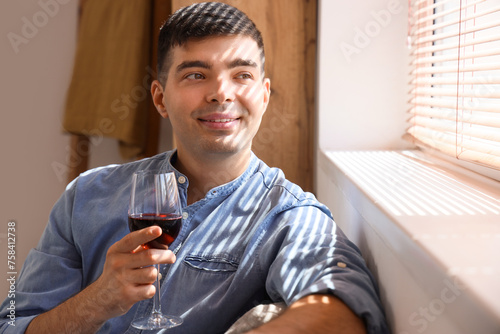 Young man with glass of red wine at home, closeup