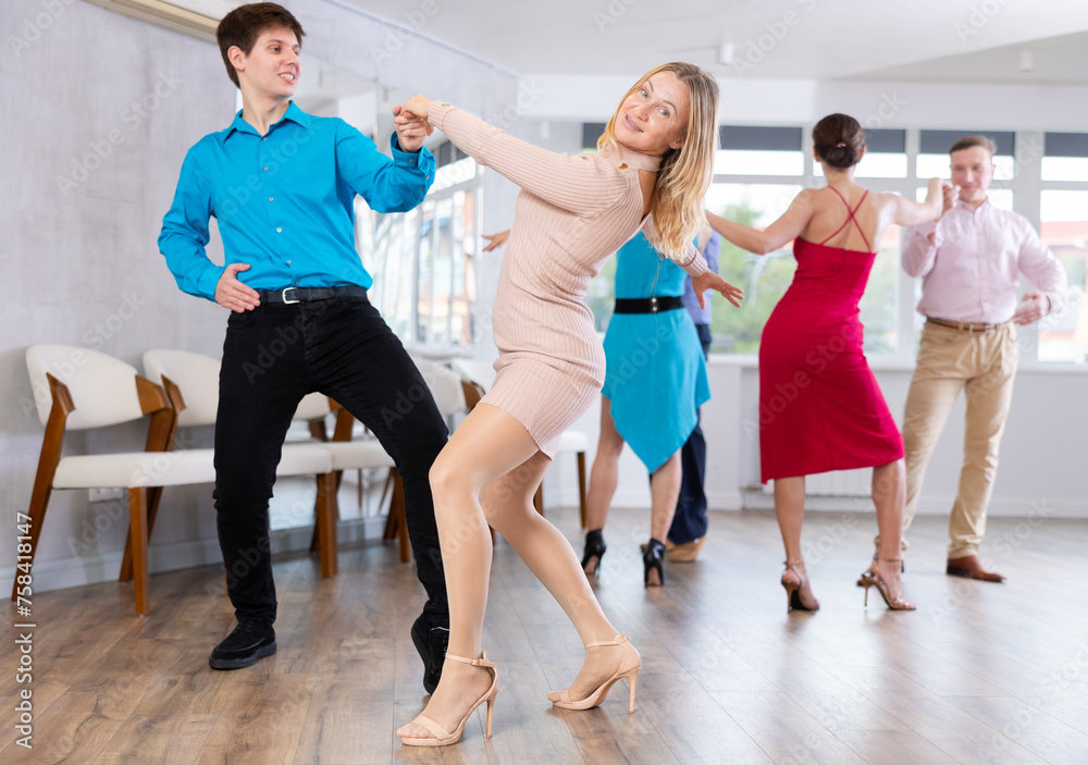 Positive adult pairs practicing vigorous jive movements in dance class