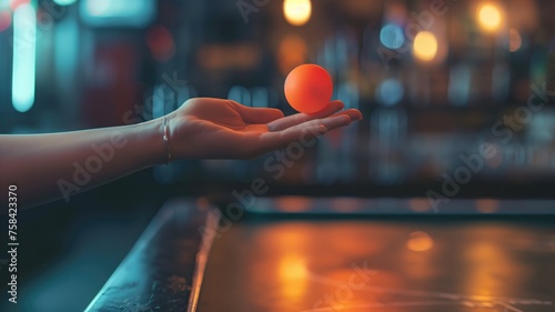 Hand delicately balancing a bright orange ping pong ball, focus and stability in a dim bar photo
