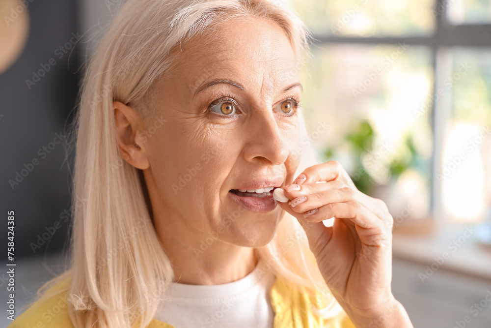 Mature woman taking pill at home, closeup