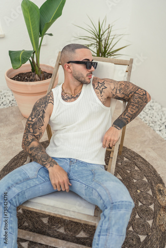 Chico joven tatuado y fitness sentado en silla en piscina de hotel
