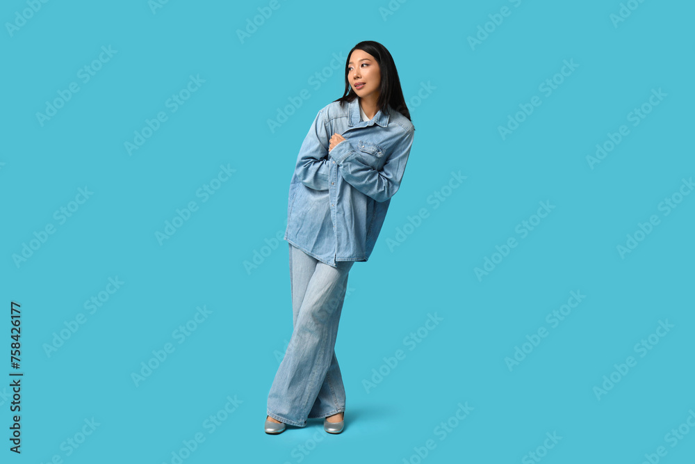 Beautiful young Asian woman in stylish denim clothes on blue background