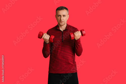 Portrait of sporty middle-aged man exercising with dumbbells on red background