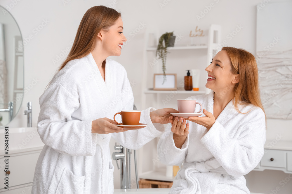 Young woman with her mother drinking coffee after shower in bathroom Young woman with her mother drinking coffee after shower in bathroom