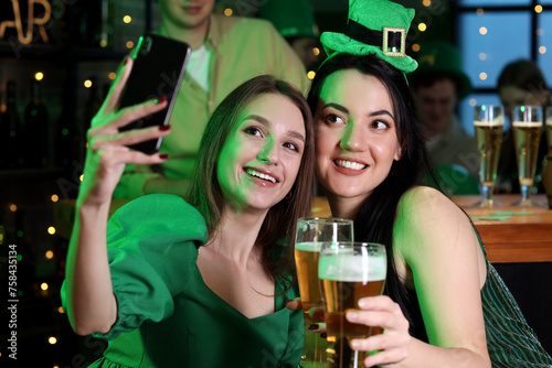 Young women with beer taking selfie in pub on St. Patrick's Day