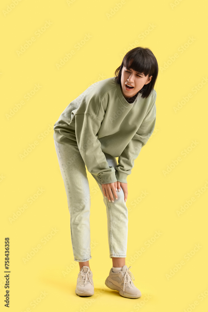 Young woman suffering from knee pain on yellow background Young woman suffering from knee pain on yellow background