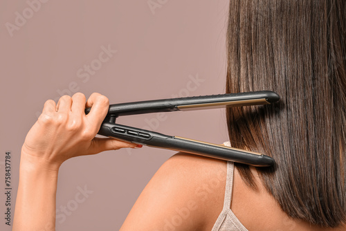 Beautiful young woman with hair straightener on pink background, closeup