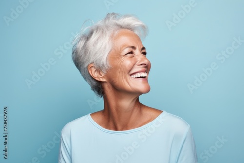 Close up portrait of a happy senior woman laughing against blue background.