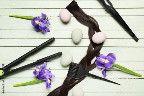 Hair strand with hairdressing accessories, flowers and Easter eggs on green wooden background