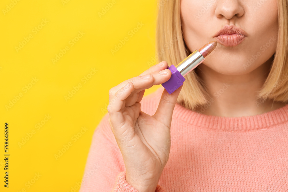 Woman applying lipstick against yellow background Woman applying lipstick against yellow background
