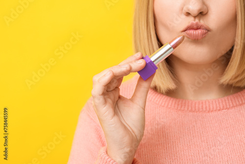 Woman applying lipstick against yellow background