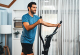 Athletic and sporty man running on elliptical running machine during home body workout exercise session for fit physique and healthy sport lifestyle at home. Gaiety home exercise workout training.