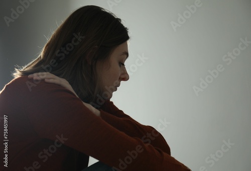 Sad young woman near grey wall indoors, space for text