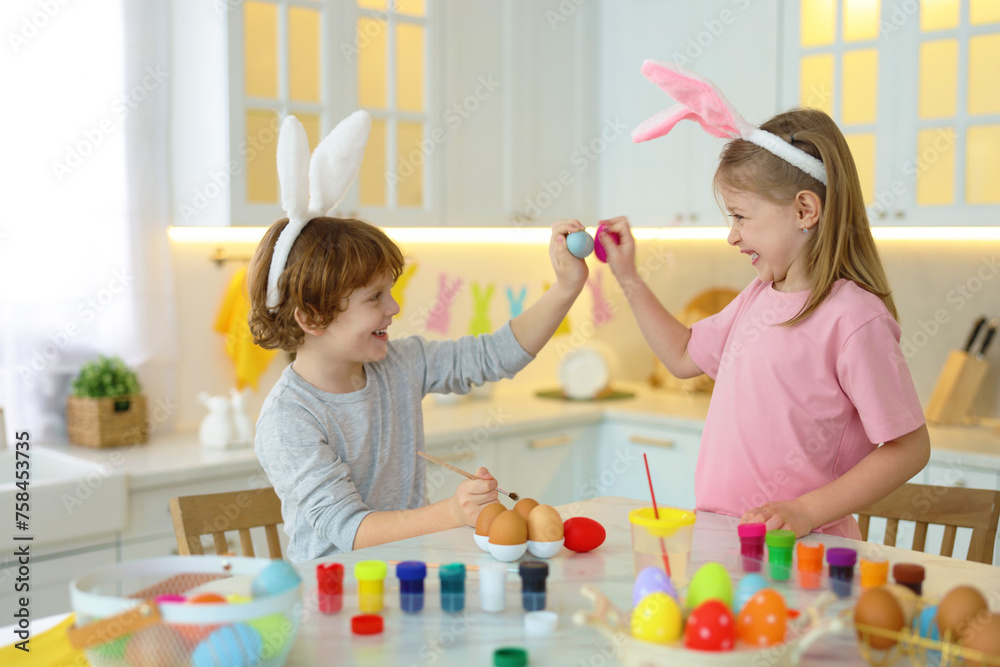 Fototapeta premium Easter celebration. Cute children with bunny ears having fun while painting eggs at white marble table in kitchen