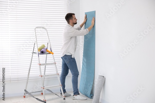 Man hanging light blue wallpaper in room © New Africa