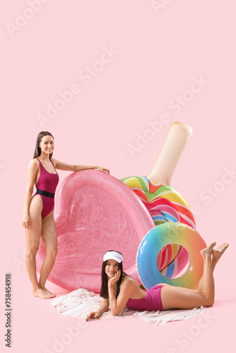 Female friends in beachwear with swim mattresses on pink background © Pixel-Shot