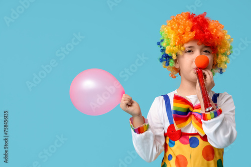 Funny little boy in clown costume with party whistle and balloon on blue background. April Fools Day celebration