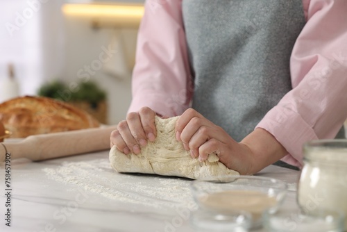 Making bread. Woman kneading dough at white table in kitchen, closeup