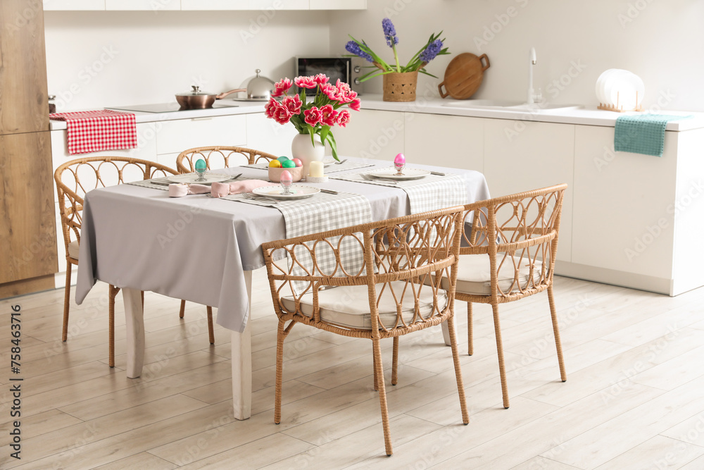 Dining table with Easter eggs, tulips and dinnerware in kitchen Dining table with Easter eggs, tulips and dinnerware in kitchen