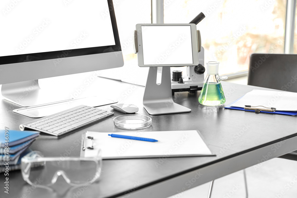 Blank tablet computer with chemistry flask on table in laboratory, closeup Blank tablet computer with chemistry flask on table in laboratory, closeup