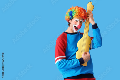 Portrait of clown playing toy guitar on blue background. April Fool s day celebration