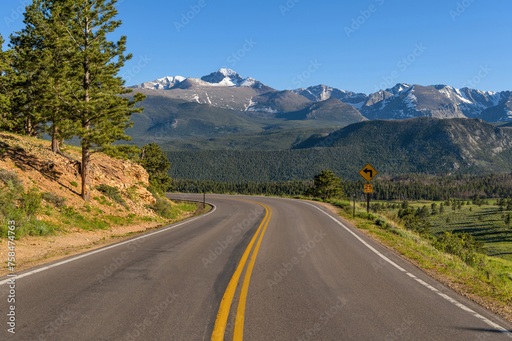 Fototapeta premium U.S. Route 36 in RMNP - A Spring evening view of winding Highway 36, with snow-capped Longs Peak towering in background, in Rocky Mountain National Park, Colorado, USA.