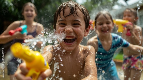 A group of children with various special needs are playing in a backyard with their siblings and parents. They are having a fun water fight with water guns and hoses and everyone © Justlight