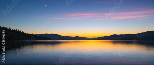 Tranquil lake’s coast as the sun dips below the horizon, casting vibrant yellow rays across the reflective surface.