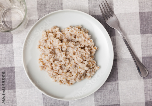 Boiled pearl barley served on ceramic dish on checkered fabric surface