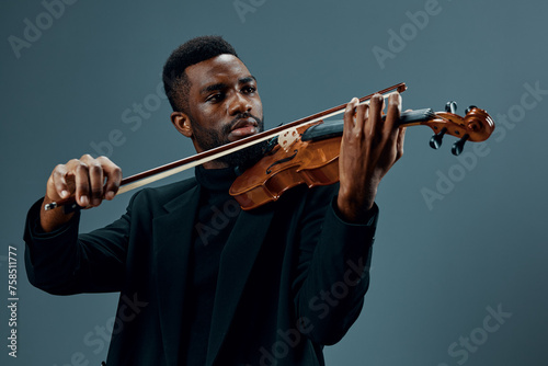 Soulful African American musician in black suit playing violin on gray background in elegant musical performance