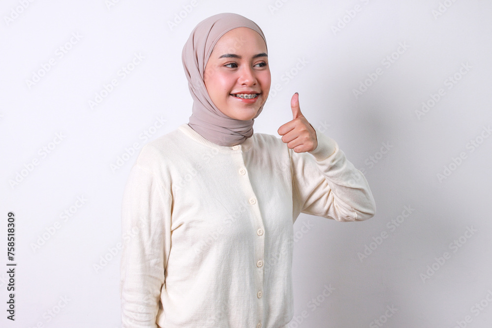 Young Asian moslem woman with braces and hijab showing thumbs up with happy expression Young Asian moslem woman with braces and hijab showing thumbs up with happy expression