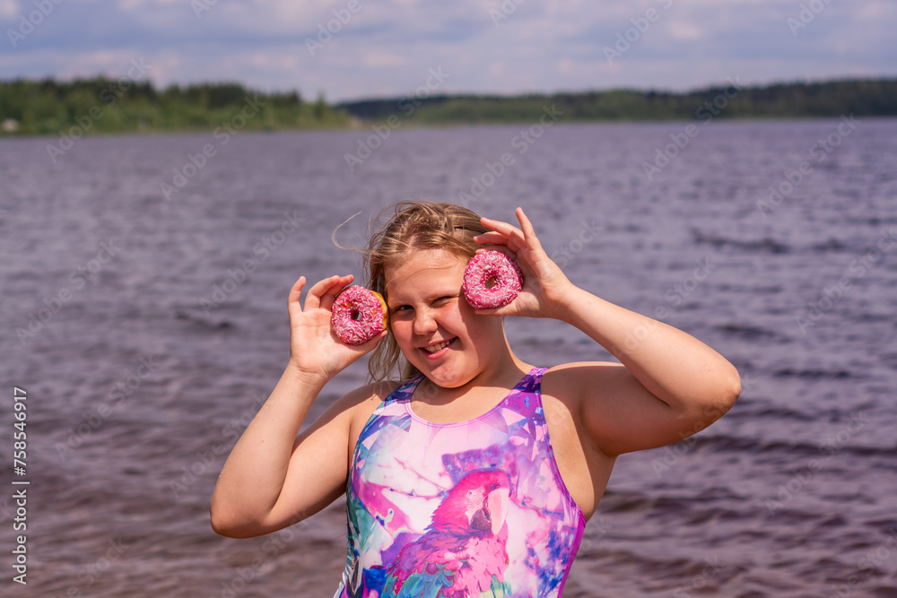 On a hot summer day, a child is relaxing on the lake. A girl on the beach. The girl is holding a pink donut in her hands.