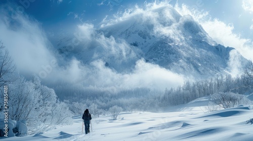 A solitary trekker stands amidst a snowy landscape, gazing at a fog-enshrouded mountain under a clear blue sky.