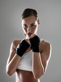 Serious woman, portrait and boxer with fist straps in fitness, fight or workout exercise on a gray studio background. Young female person or fighter ready for practice, competition or sports training