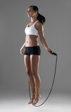 Woman, fitness and jumping with rope in cardio workout, exercise or training on a gray studio background. Active female person or athlete skipping in balance, challenge or weight loss on mockup space