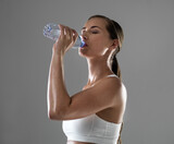 Woman, fitness and drinking with water for hydration after workout or exercise on a gray studio background. Thirsty female person or athlete with bottle of liquid for natural sustainability on mockup